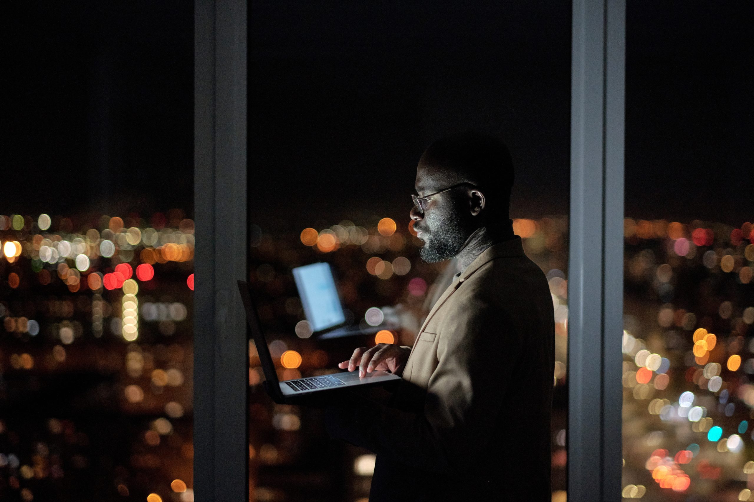 Young businessman with laptop standing against large window in office