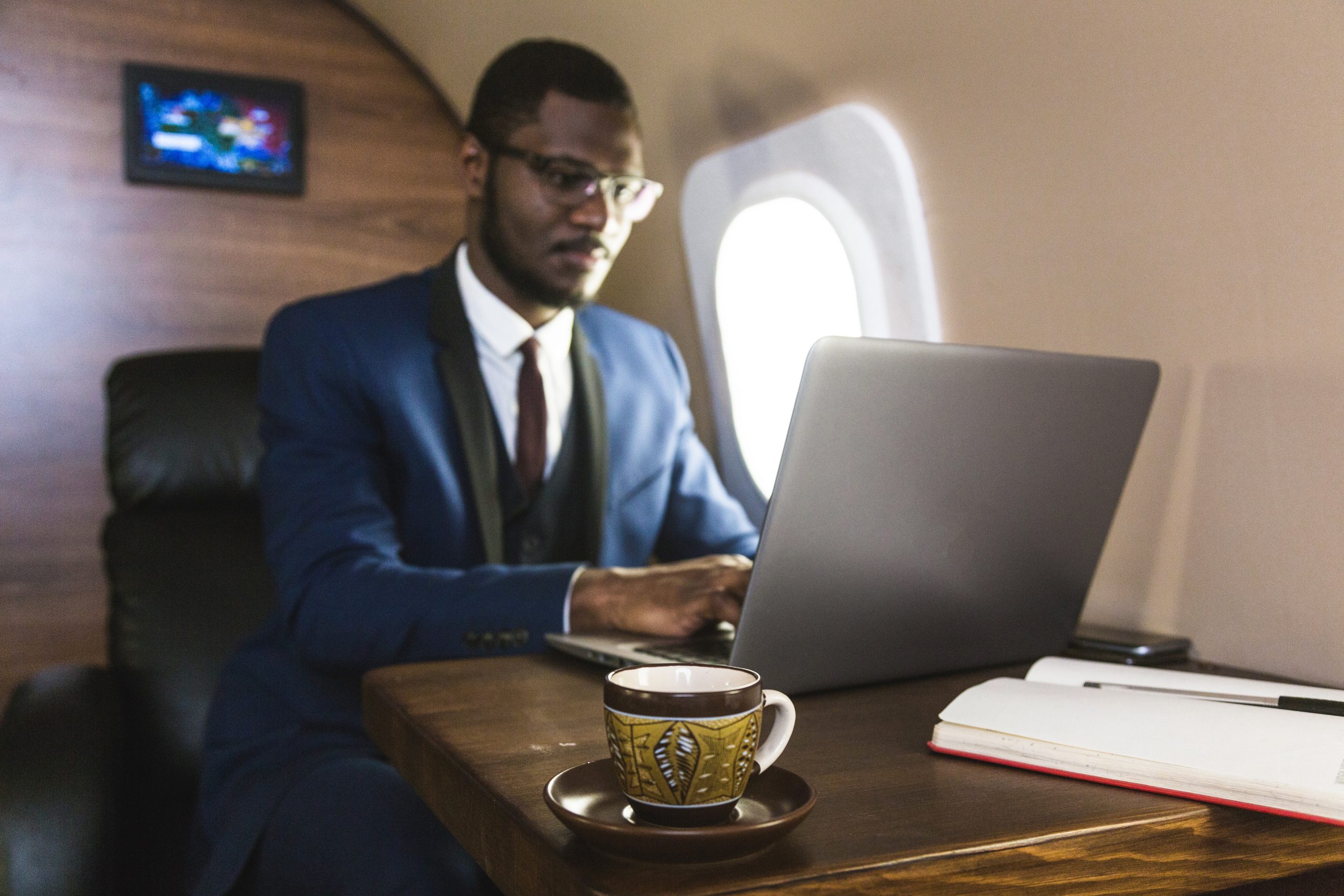 Attractive and successful African American businessman with glasses working on a laptop while sitting in the chair of his private jet.