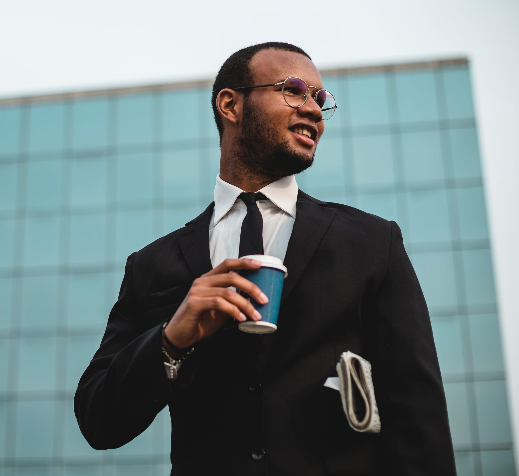 Businessman with takeaway coffee in front of the skyscraper.