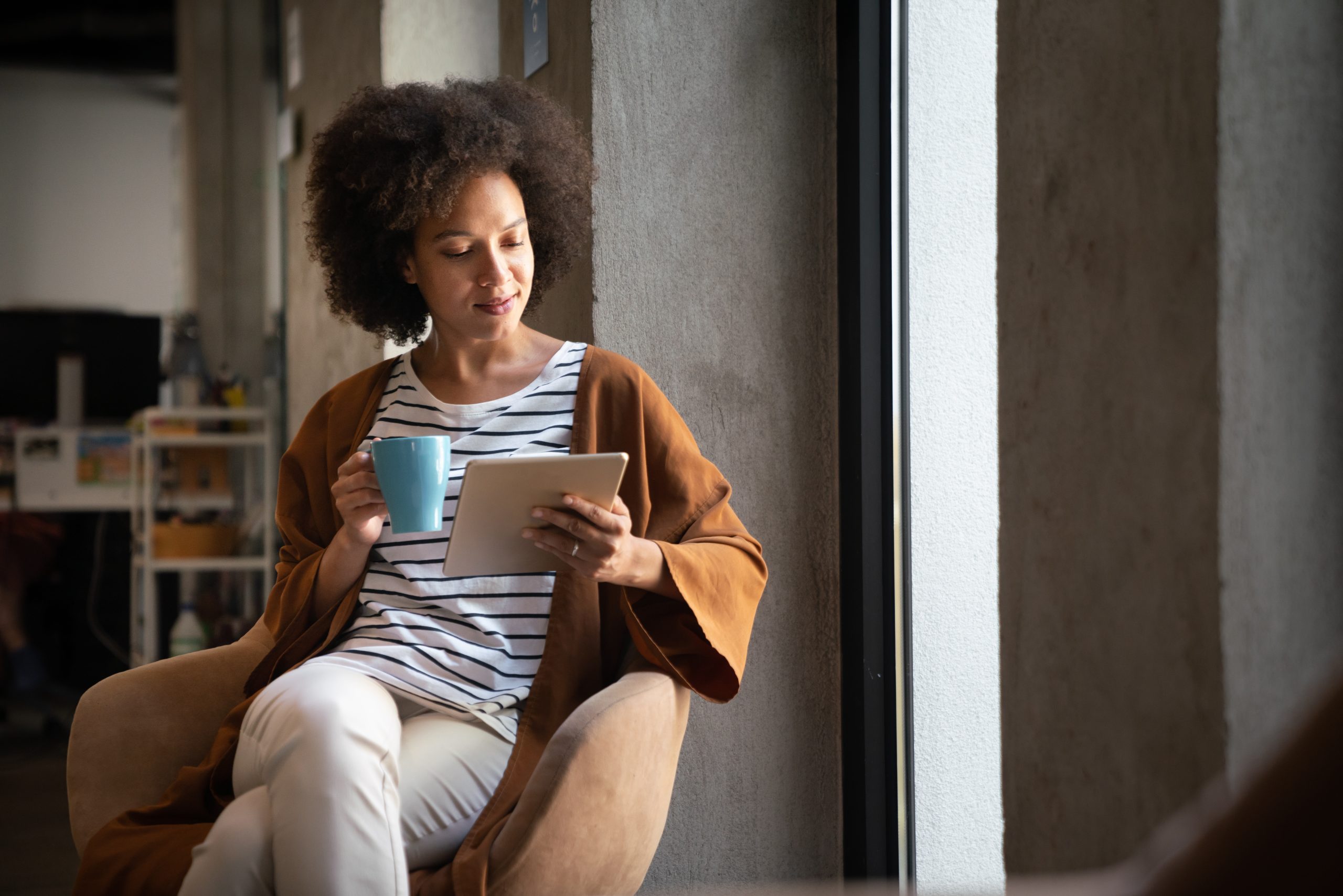 Enjoying coffee break with tablet. Attractive black business woman working on digital tablet