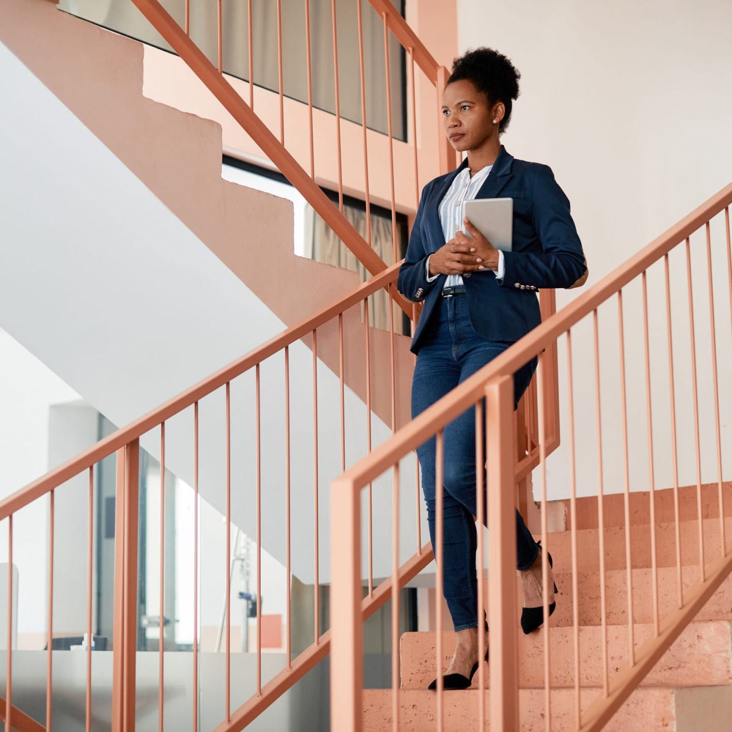 African American businesswoman holding digital tablet while walking down the stairs at work. Copy space.