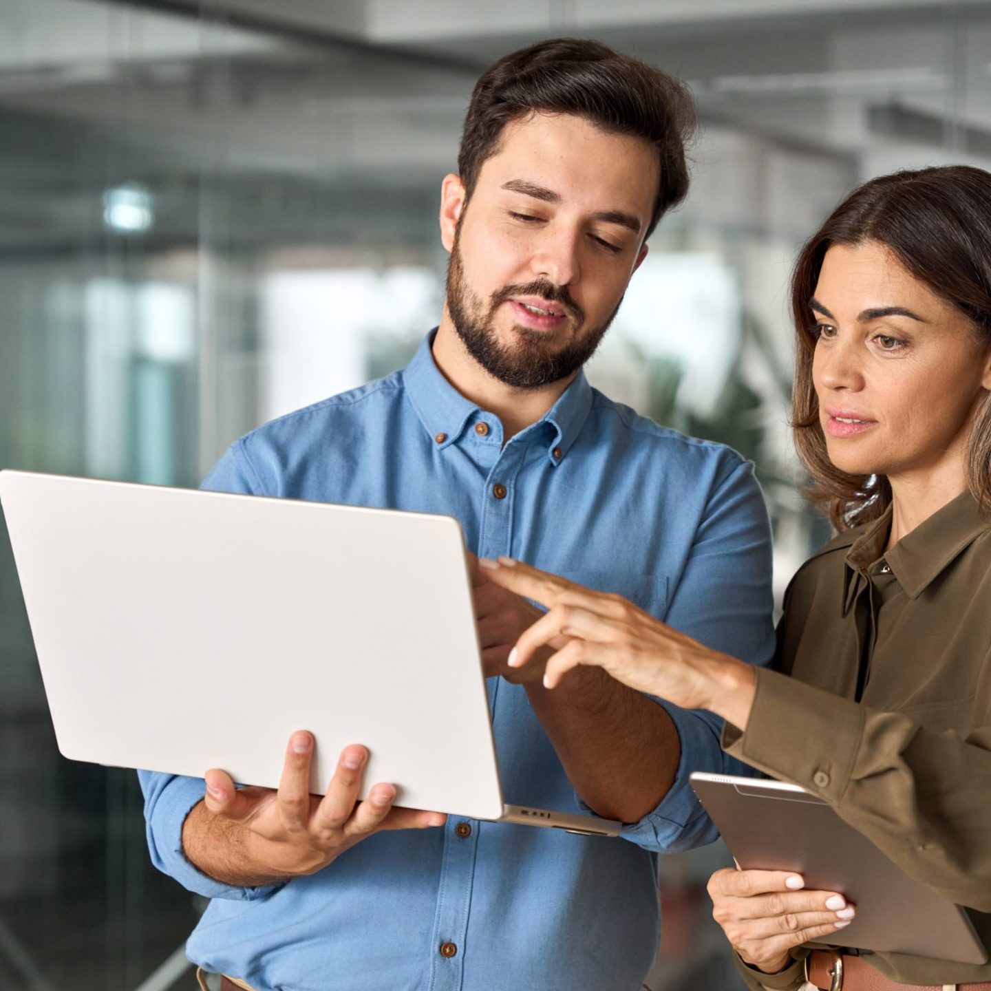 Two busy professional business people working in office with computer. Middle aged female executive manager talking to male colleague having conversation showing software online solution on laptop.