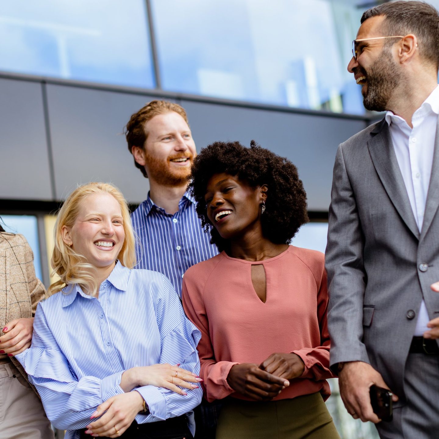 A group of businness people colleagues gathers for a casual conversation outside a contemporary office, reflecting teamwork and connection.