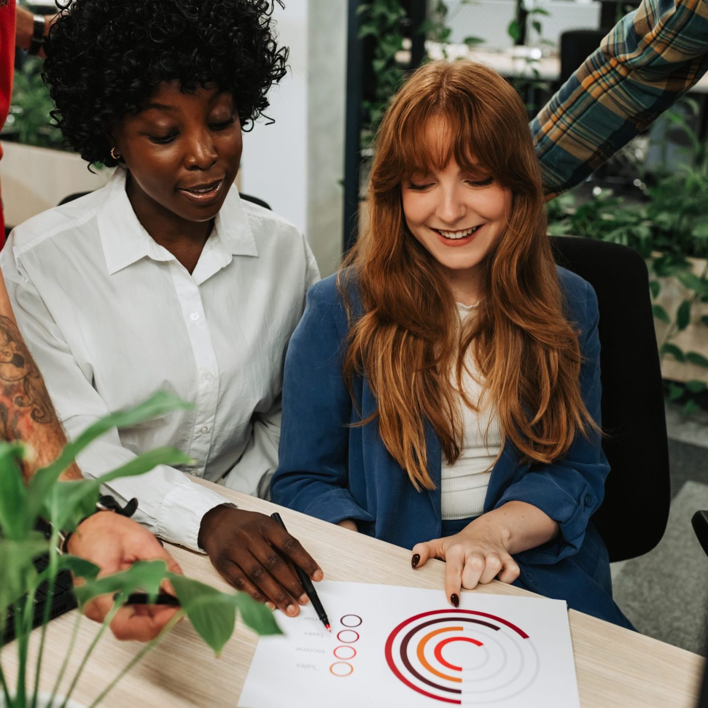 An interracial team of four experts sitting at office and doing statistics while analyzing chart. A businesspeople working on paperwork and documentation while discussing their current project.